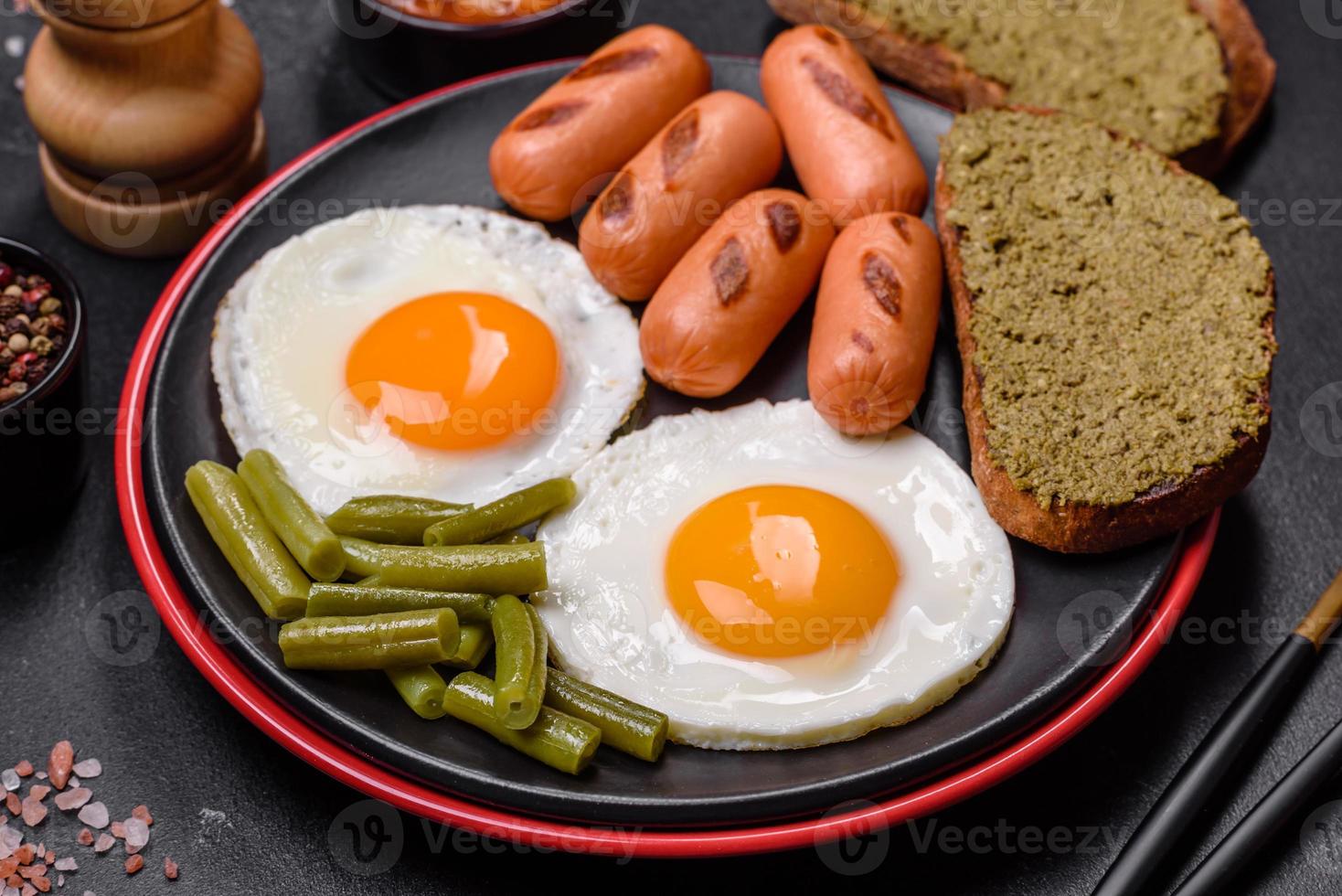 smakelijk Engels ontbijt van gebakken eieren, bonen, asperges, worstjes met specerijen en kruiden foto