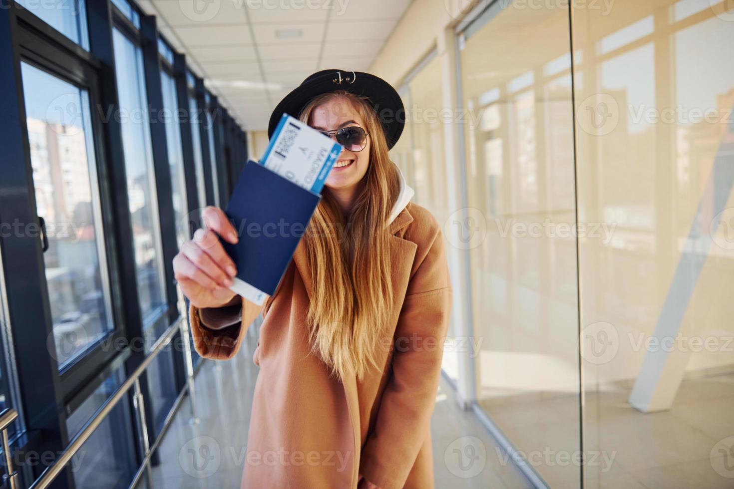 jong vrouw passagier in warm kleren tonen kaartjes in luchthaven hal foto