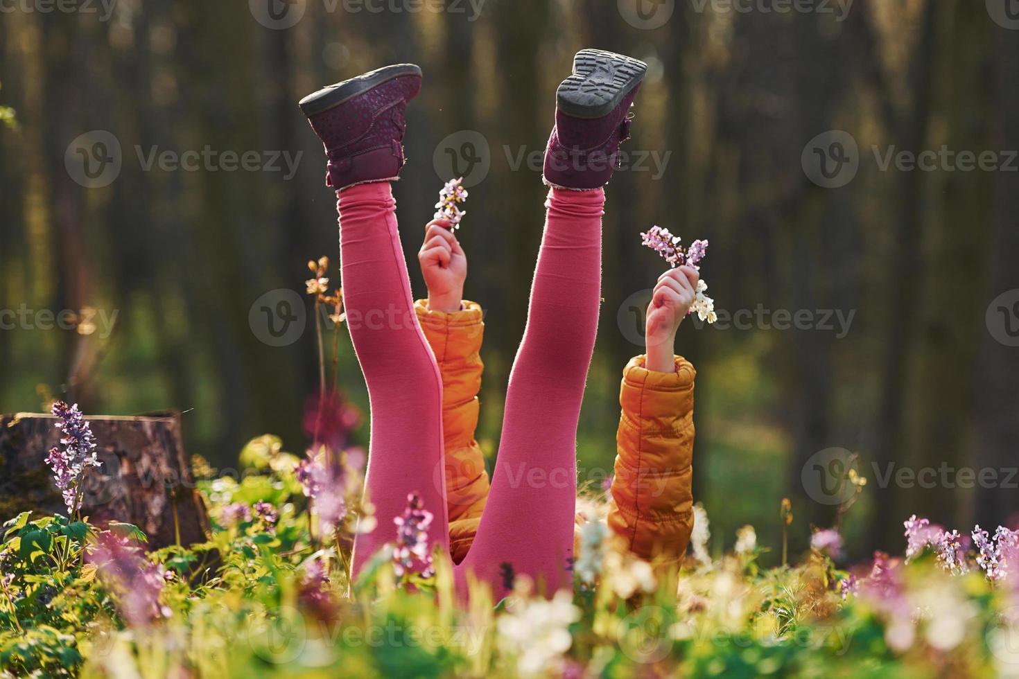 gelukkig weinig meisje in gewoontjes kleren aan het liegen naar beneden Aan grond in voorjaar Woud Bij dag foto