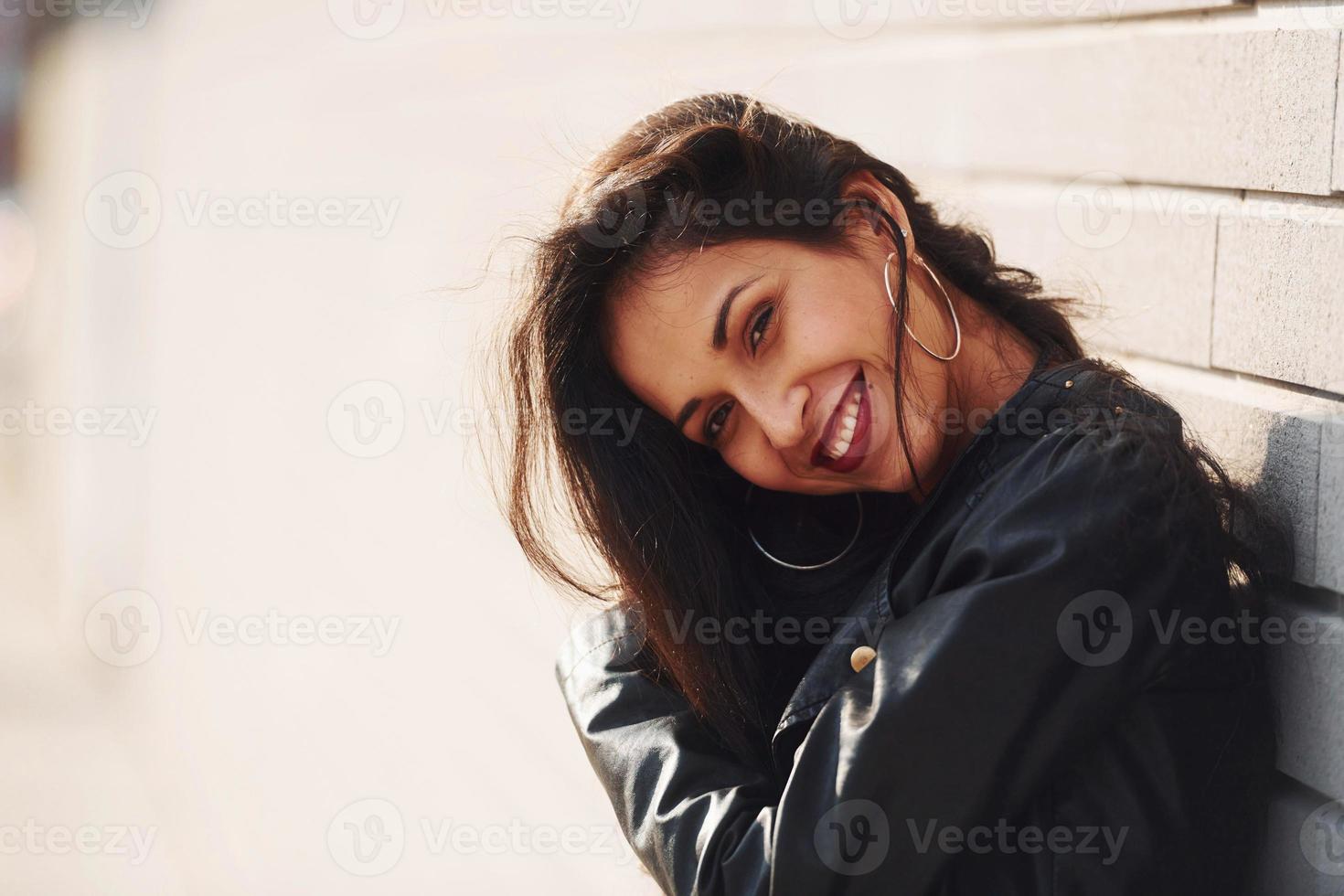 potrait van vrolijk brunette met gekruld haar- en in zwart kleren leunend Aan de muur foto