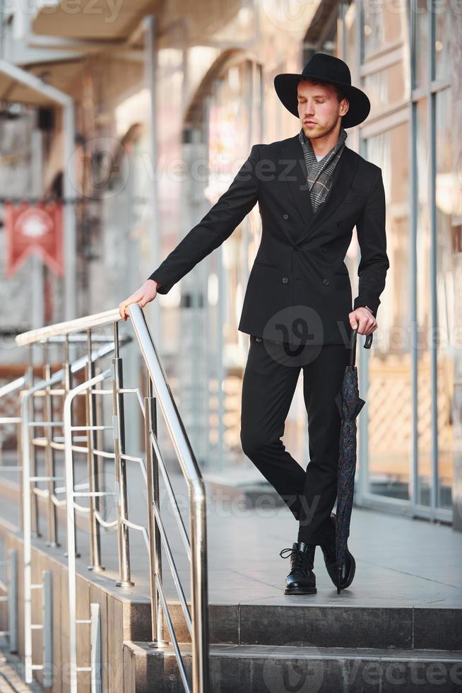 elegant jong Mens in zwart hoed en met paraplu buitenshuis in de stad foto