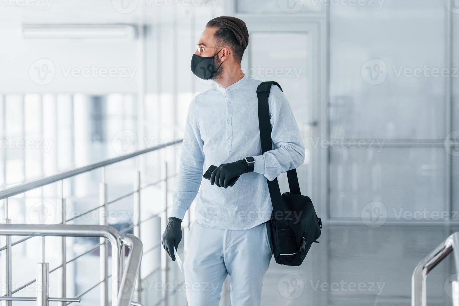 in beschermend masker en handschoenen. jong knap Mens in formeel kleren binnenshuis in de kantoor Bij dag foto