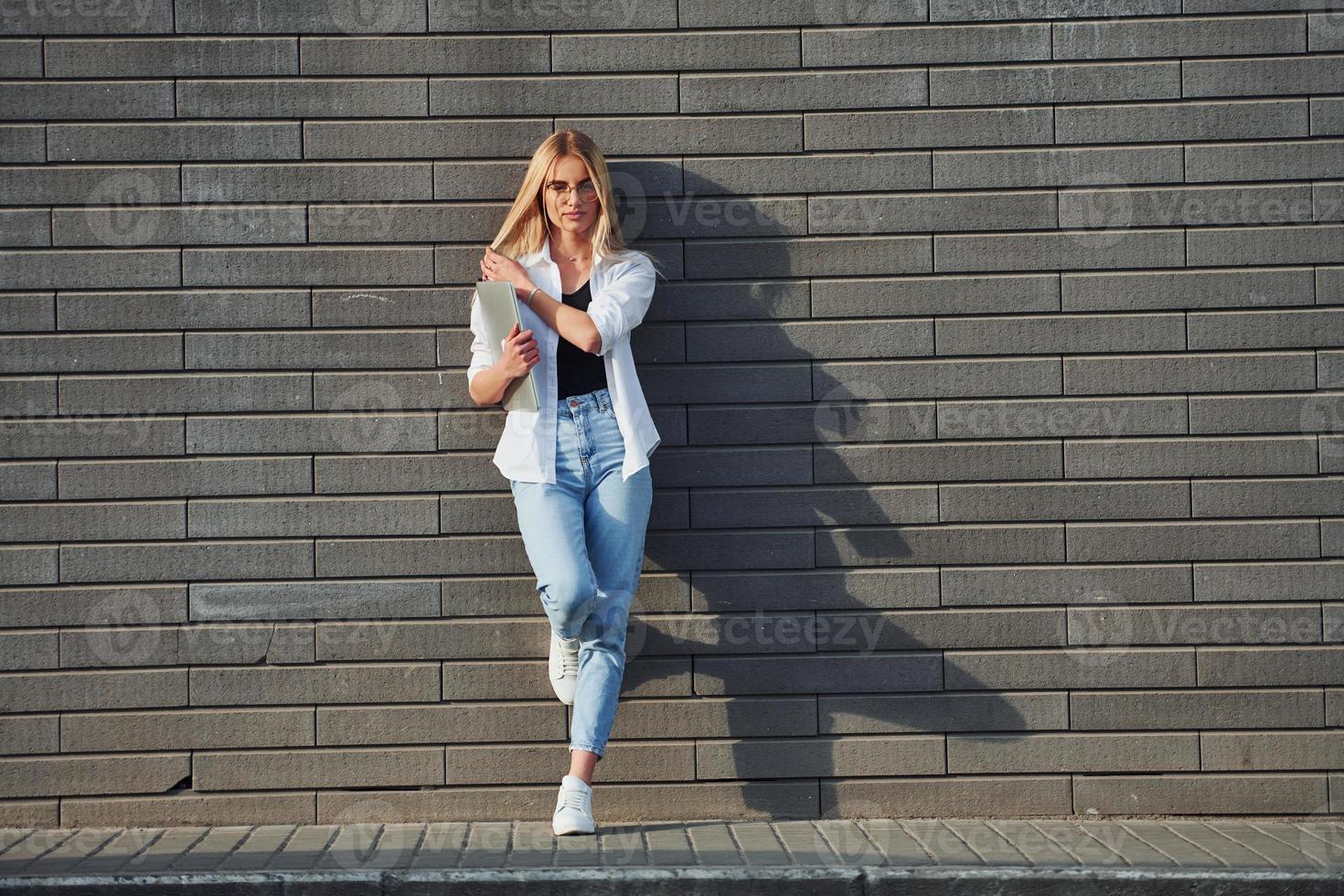 gebruik makend van laptop. mooi blond in gewoontjes kleren is buitenshuis Bij zonnig dag foto