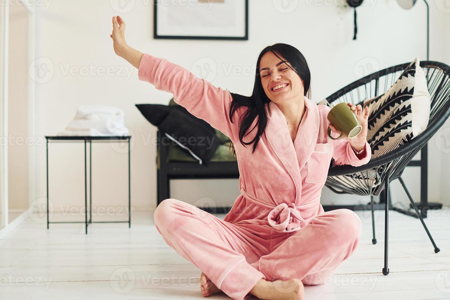 vrolijk jong vrouw in pyjama zittend Aan de verdieping binnenshuis Bij dag foto