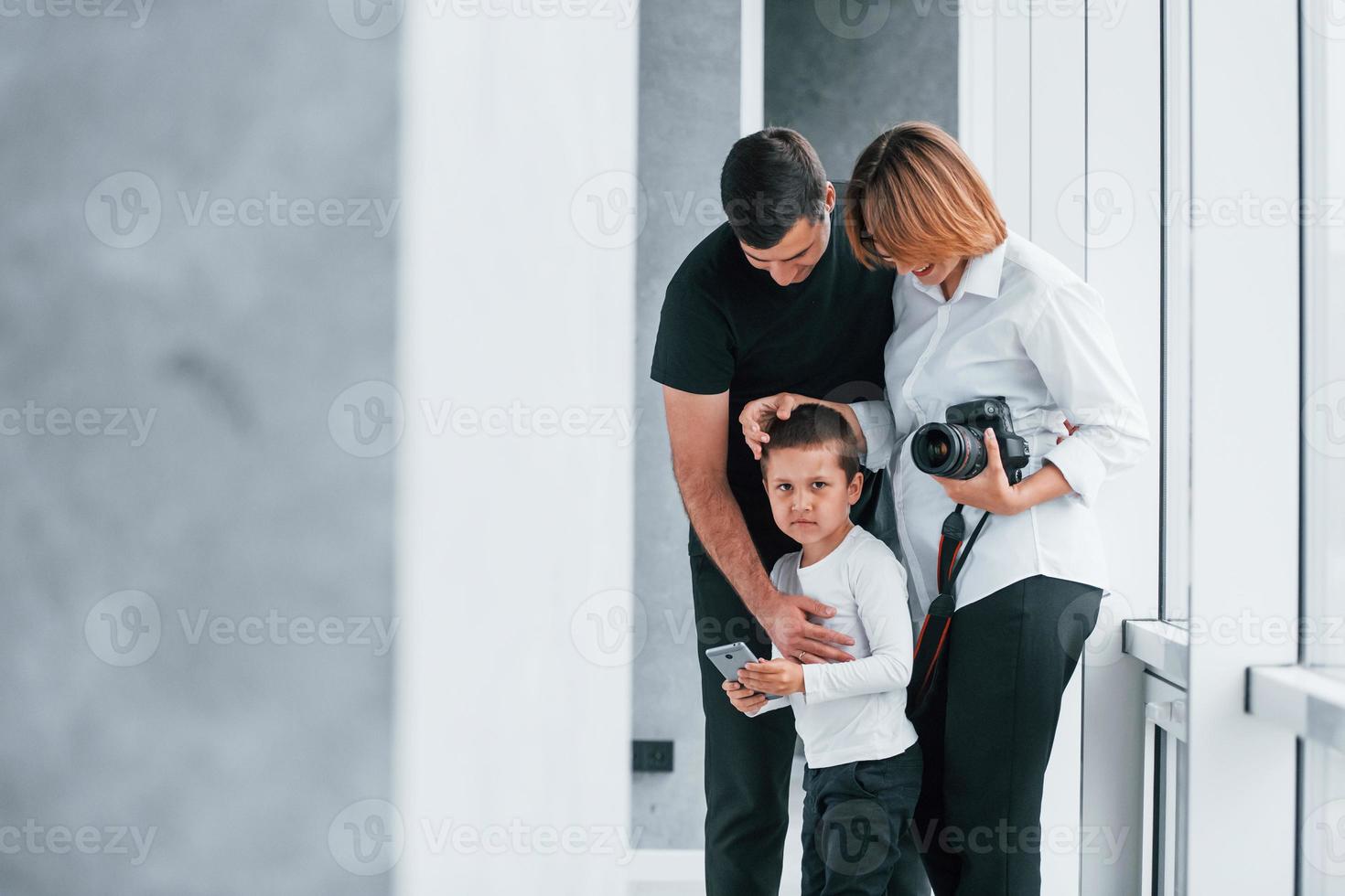 vrouw in formeel kleren en met camera in hand- staand binnen van leeg kamer met Mens en weinig jongen foto