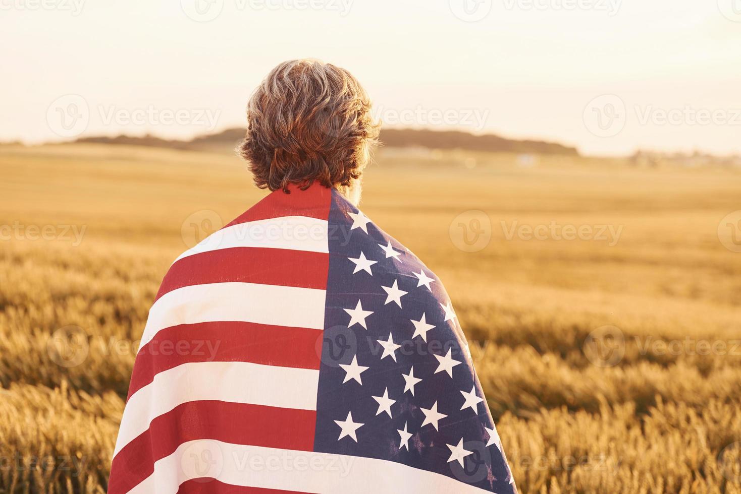 visie van achter van patriottisch senior Mens dat staand Aan de veld- met Verenigde Staten van Amerika vlag. opvatting van vrijheid foto