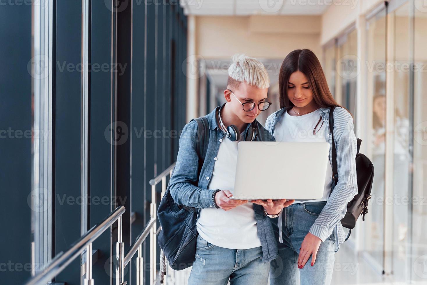 twee jong leerling vrienden samen in een gang van een college met laptop in handen foto