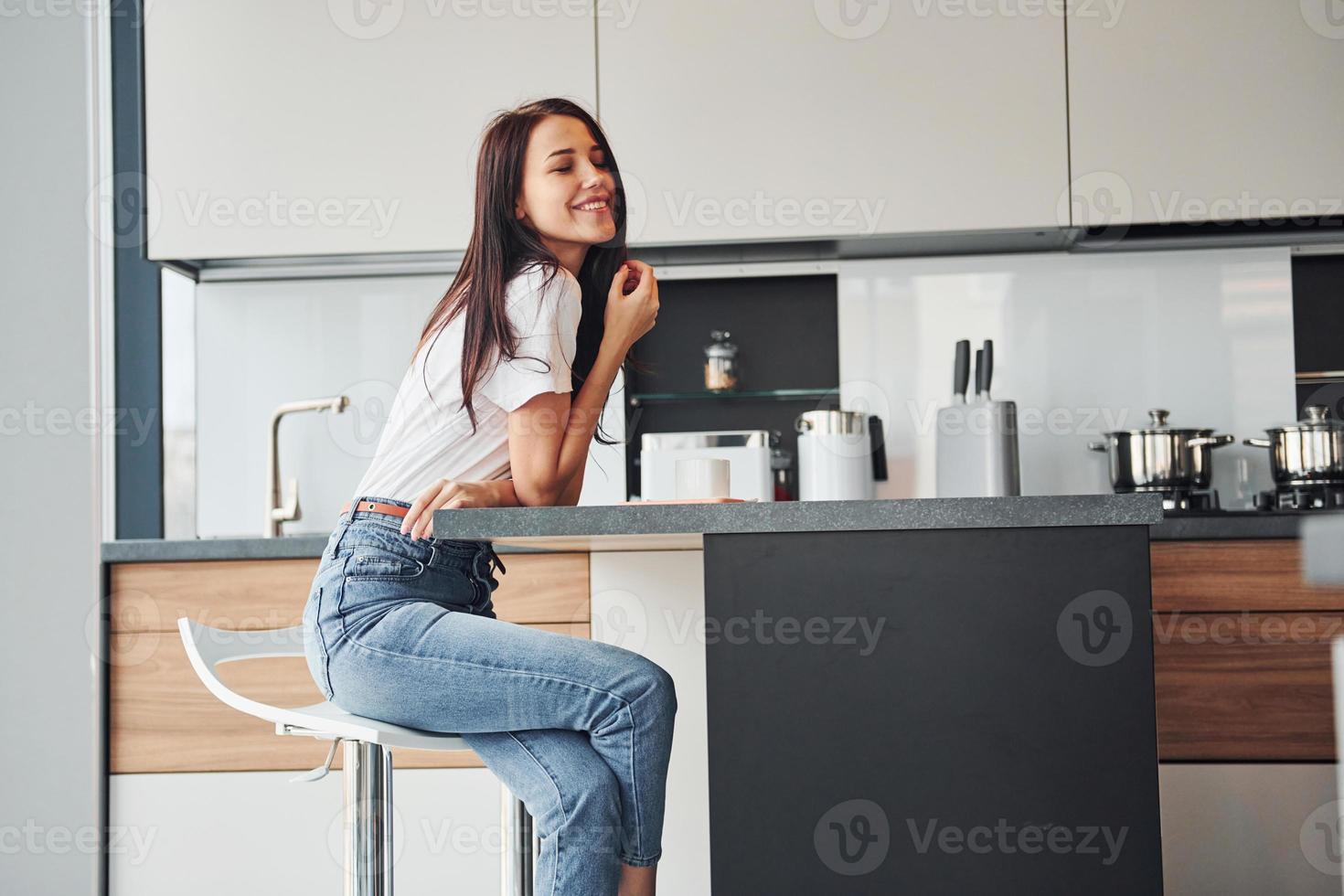 jong mooi brunette in gewoontjes kleren zit in keuken met vers drinken Bij ochtend- tijd foto