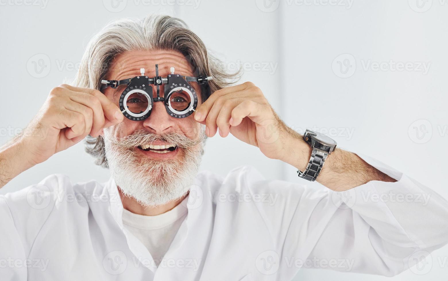 mooi hoor gelaats uitdrukkingen. senior Mens met grijs haar- en baard is in oogheelkunde kliniek foto