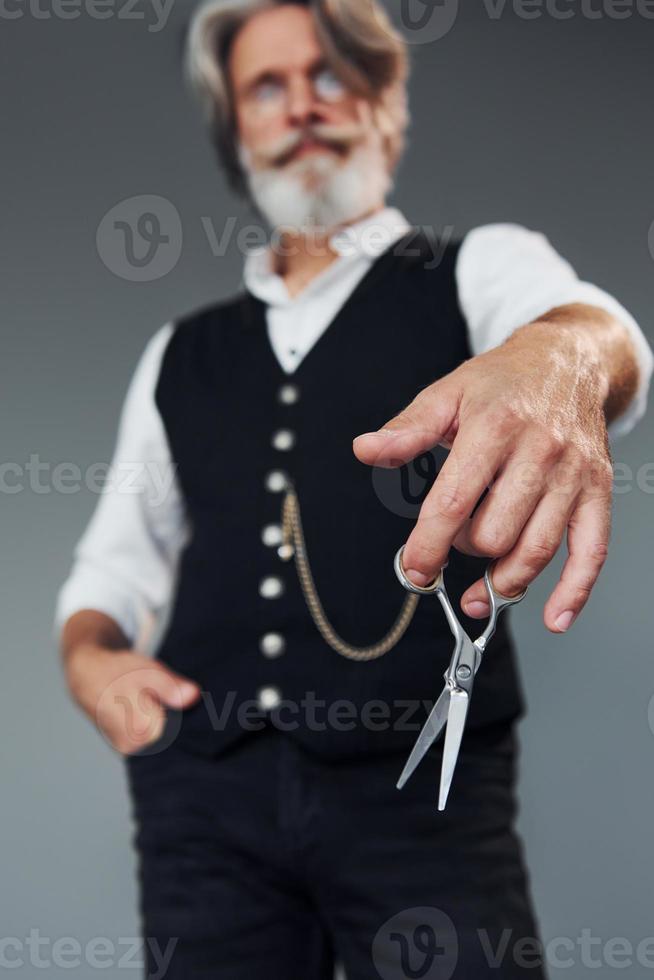 kapperszaak hulpmiddelen. tegen grijs achtergrond. elegant modern senior Mens met grijs haar- en baard is binnenshuis foto