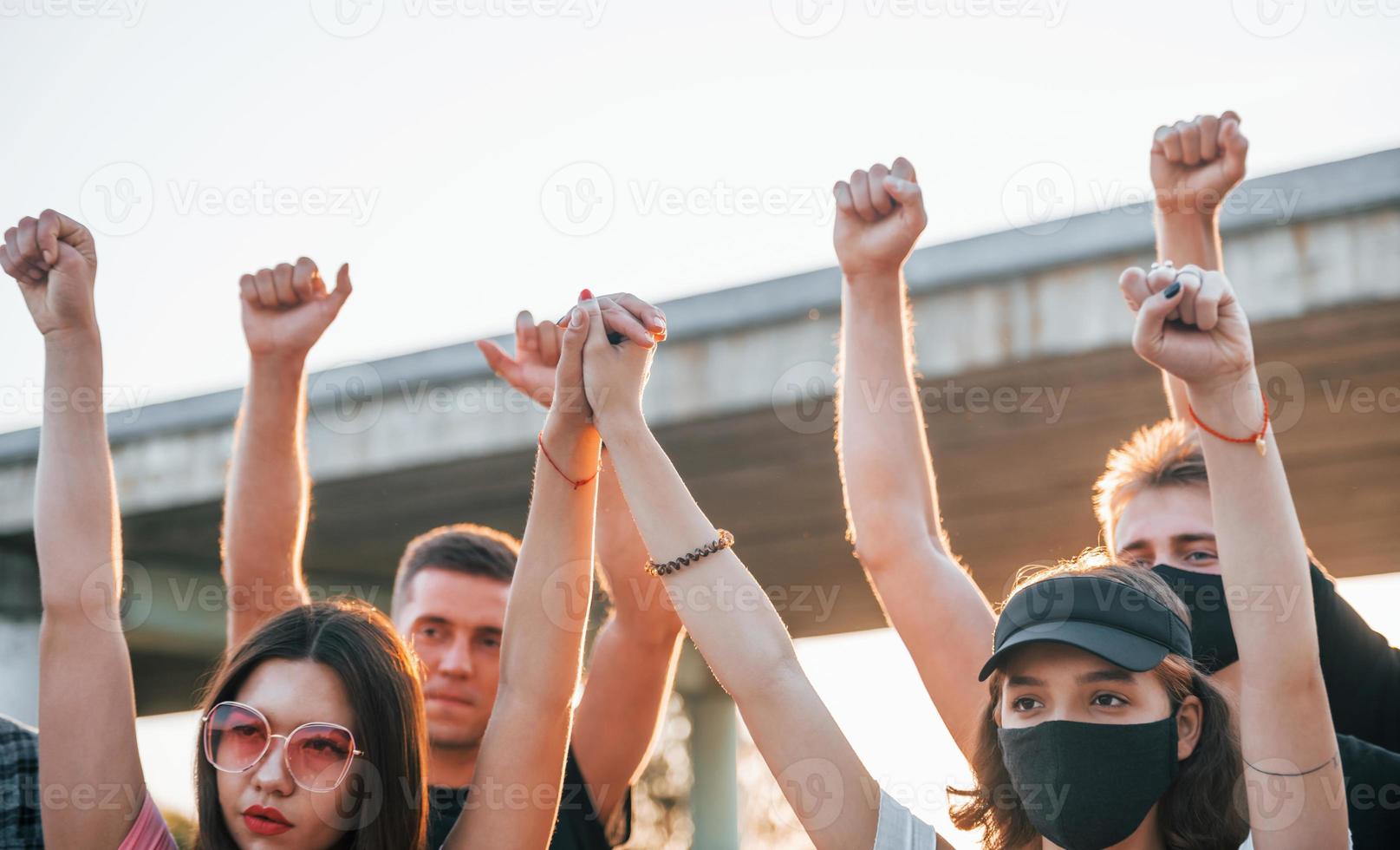 vuisten geraasd hoog omhoog. groep van protesteren jong mensen dat staand samen. activist voor menselijk rechten of tegen regering foto