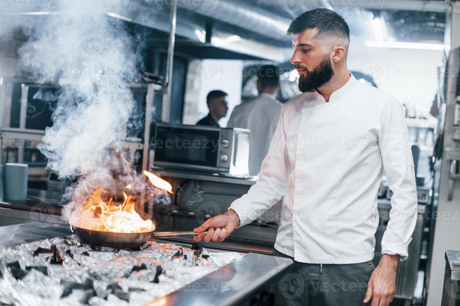 frituren pan is Aan brand. chef in wit uniform Koken voedsel Bij keuken. bezig dag Bij werk foto