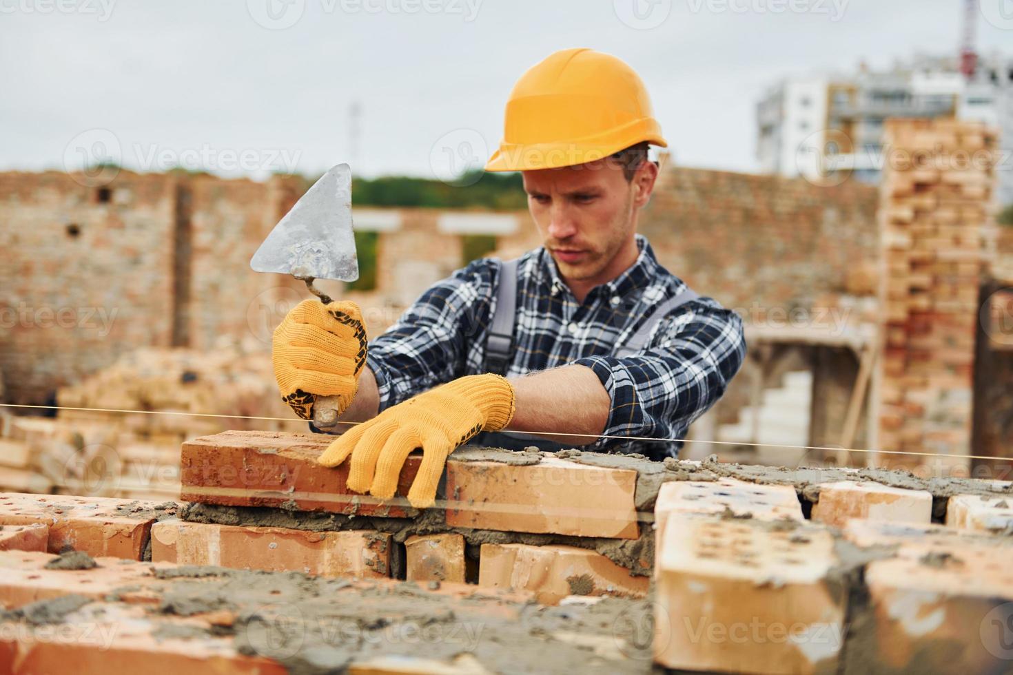 houdende bakstenen. bouw arbeider in uniform en veiligheid uitrusting hebben baan Aan gebouw foto