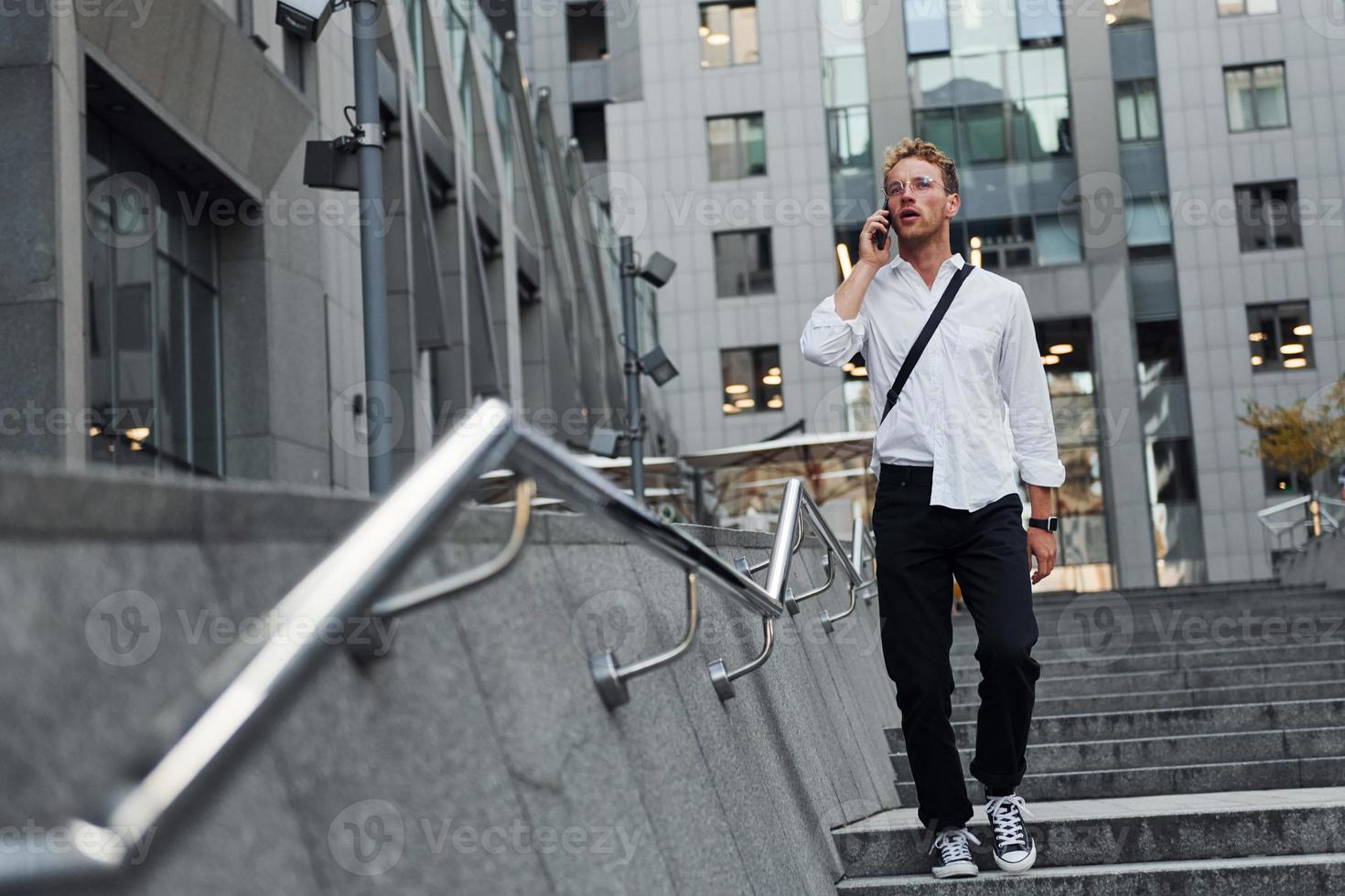 hebben gesprek door de telefoon. jong elegant Mens in mooi zo kleren is buitenshuis in de stad Bij dag foto