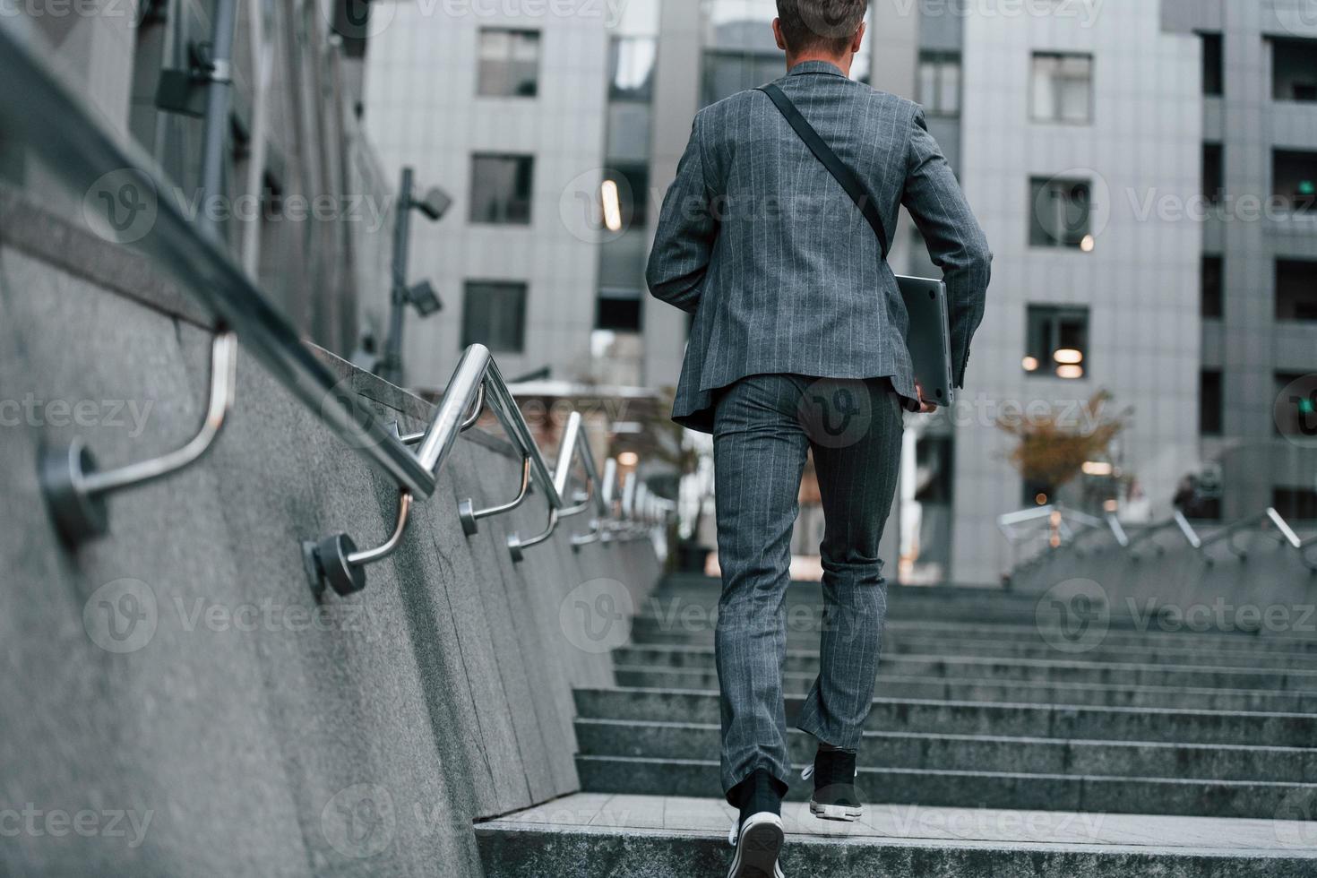 achterzijde visie. jong elegant Mens in mooi zo kleren is buitenshuis in de stad Bij dag foto