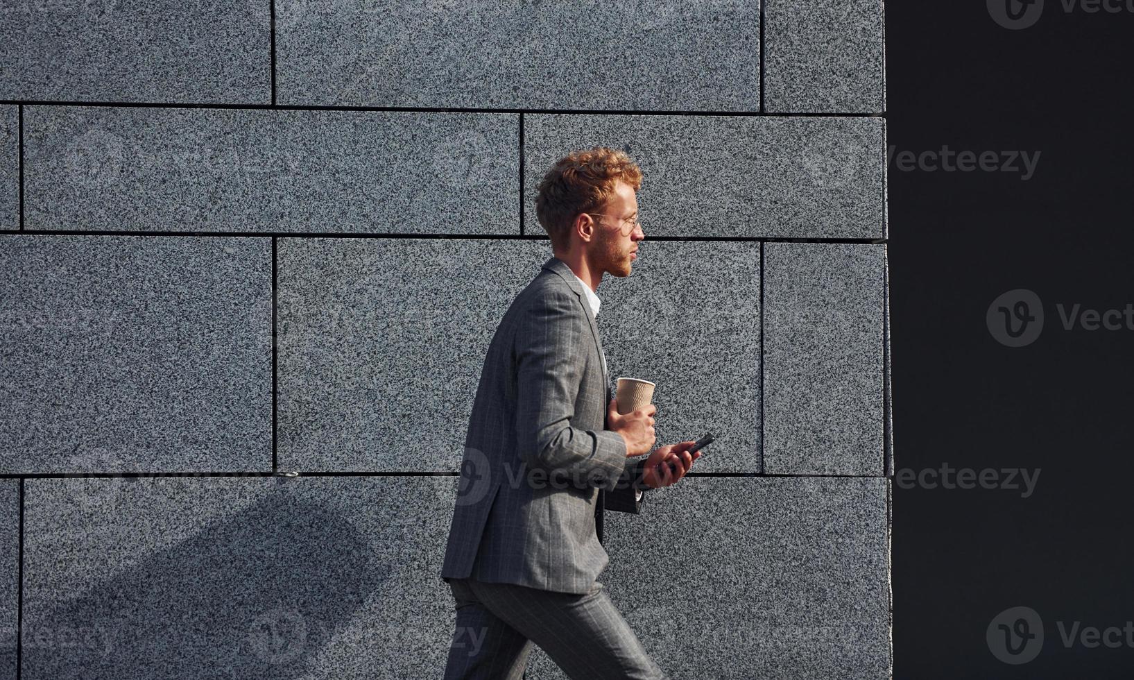 tegen grijs muur. jong zakenman in grijs formeel slijtage is buitenshuis in de stad foto