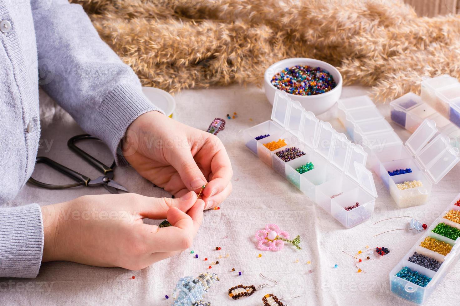 een meisje weeft een kralen armband Aan een tafel tussen dozen van kralen. kinderen s hobby foto