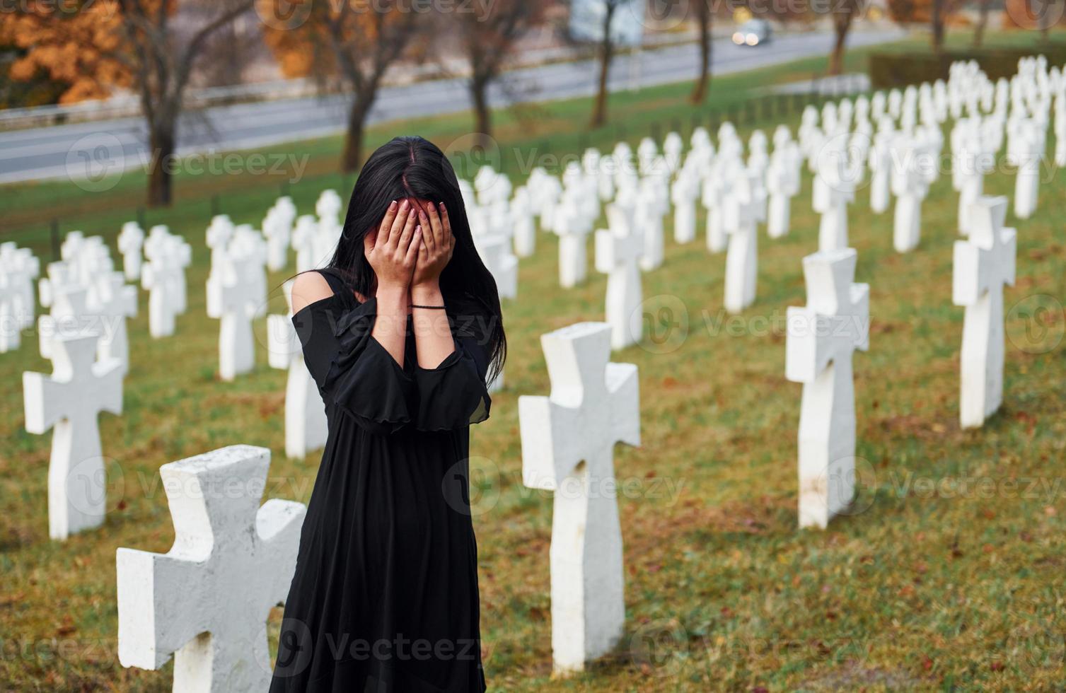jong vrouw in zwart kleren bezoekende begraafplaats met veel wit kruisen. opvatting van begrafenis en dood foto