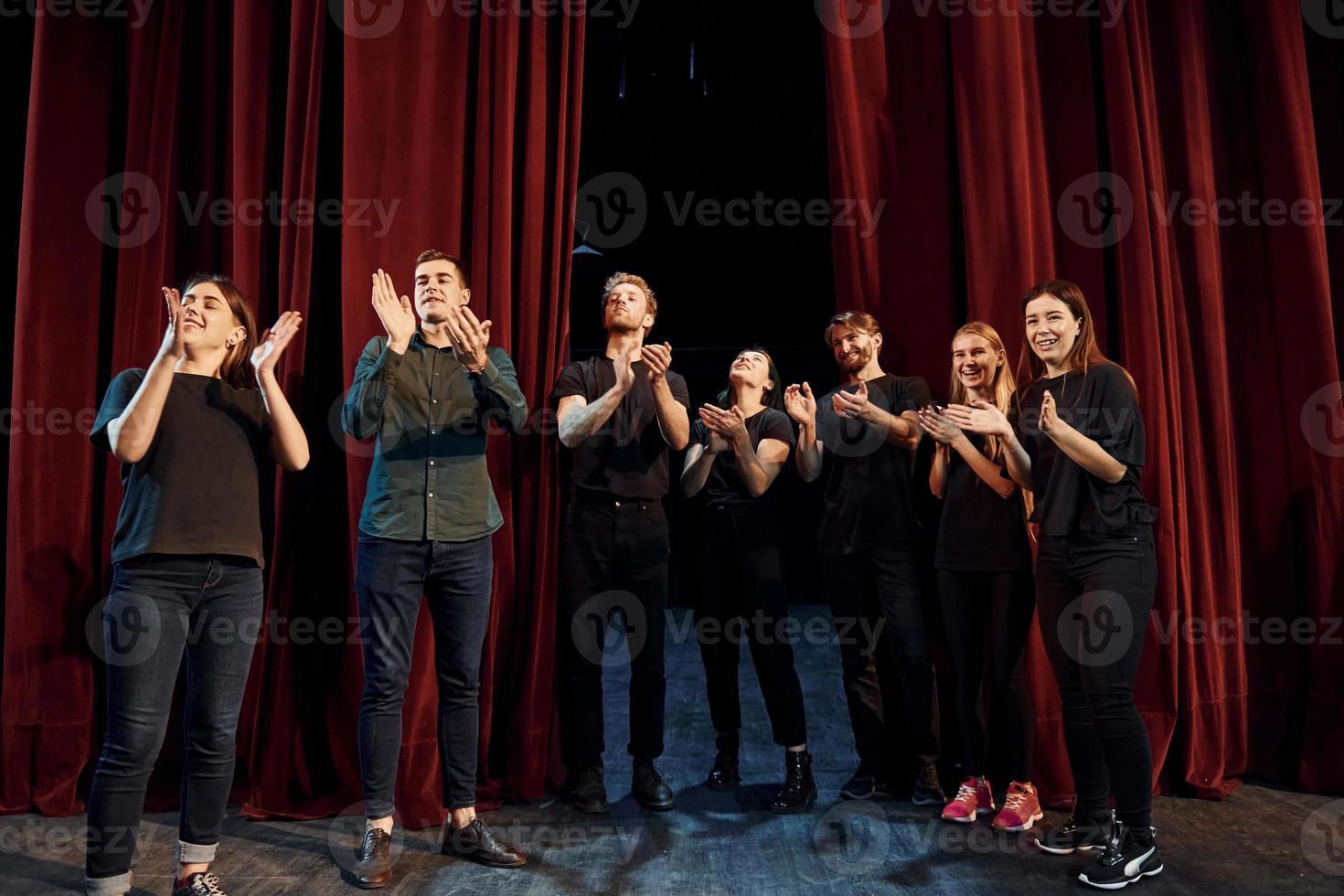 staand tegen rood gordijnen. groep van acteurs in donker gekleurde kleren Aan repetitie in de theater foto