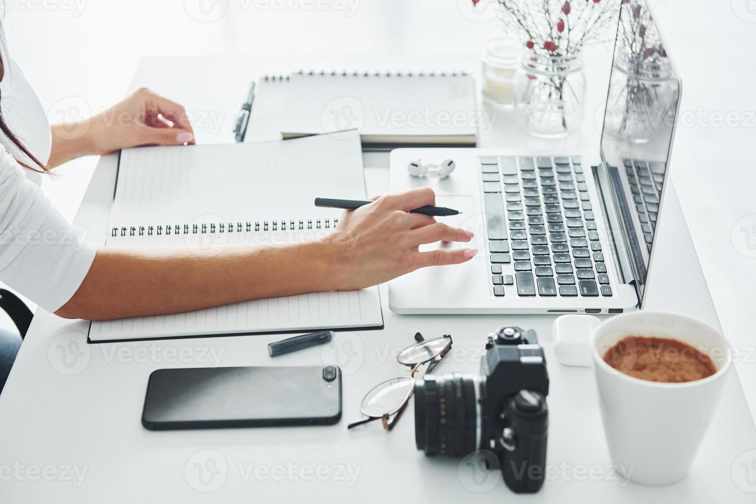 gebruik makend van laptop en kladblok. jong vrouw freelancer werken binnenshuis in de kantoor Bij dag foto