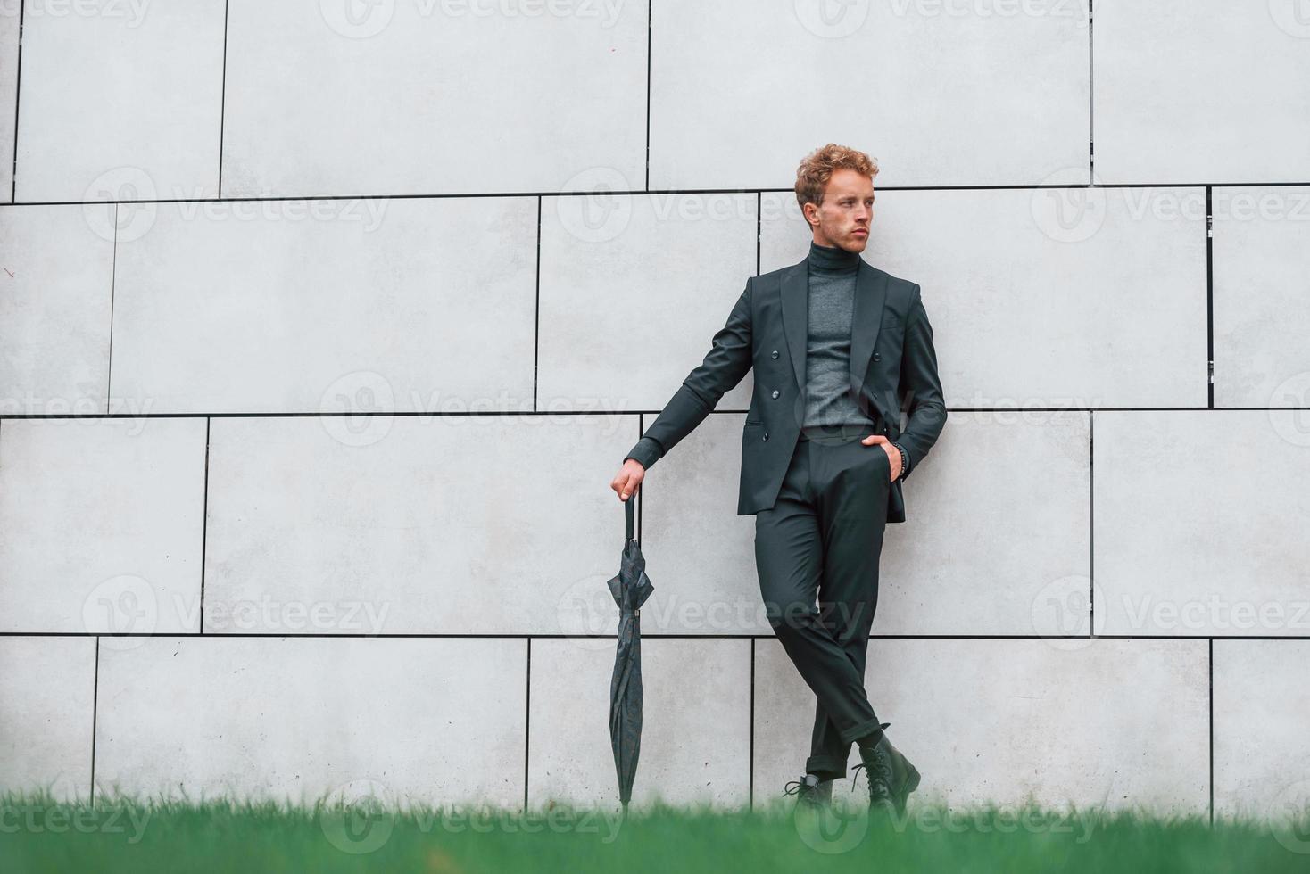 jong Mens in formeel kleren met paraplu staand in de buurt muur buitenshuis met paraplu foto