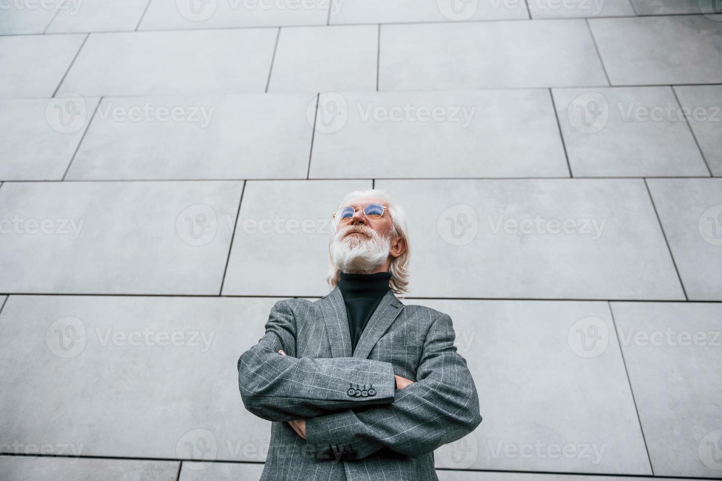 senior zakenman in formeel kleren, met grijs haar- en baard is buitenshuis staat tegen de muur foto