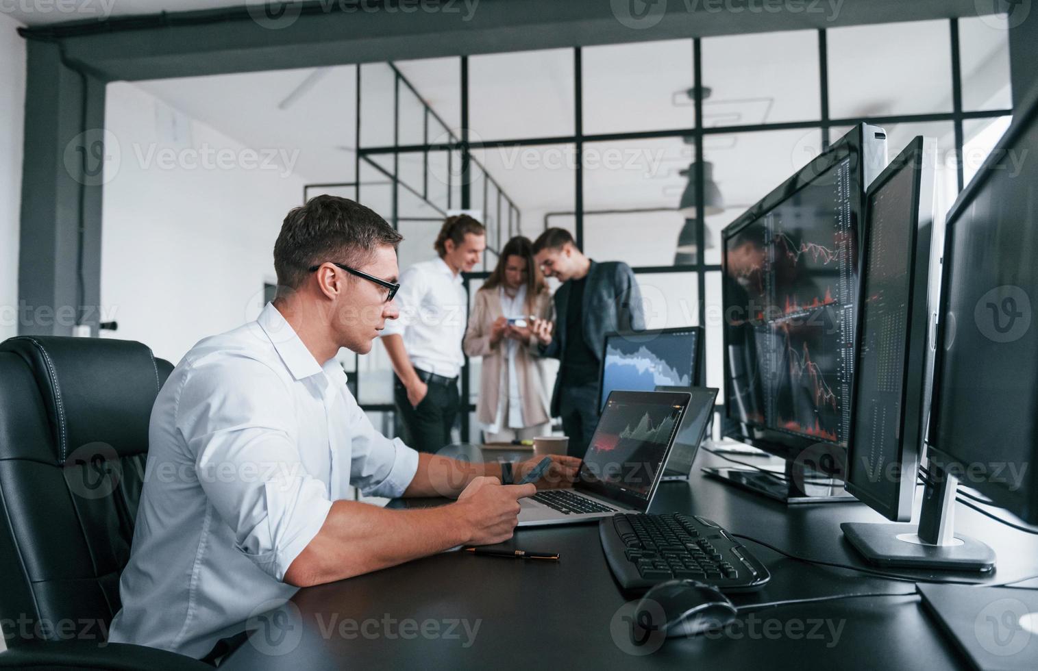 vent in bril geconcentreerd Bij werk. team van effectenmakelaars is in modern kantoor met veel Scherm schermen foto