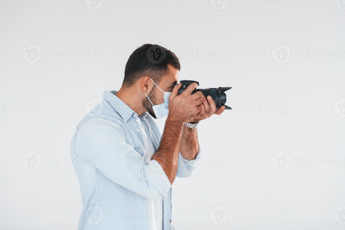 met professioneel camera. jong knap Mens staand binnenshuis tegen wit achtergrond foto