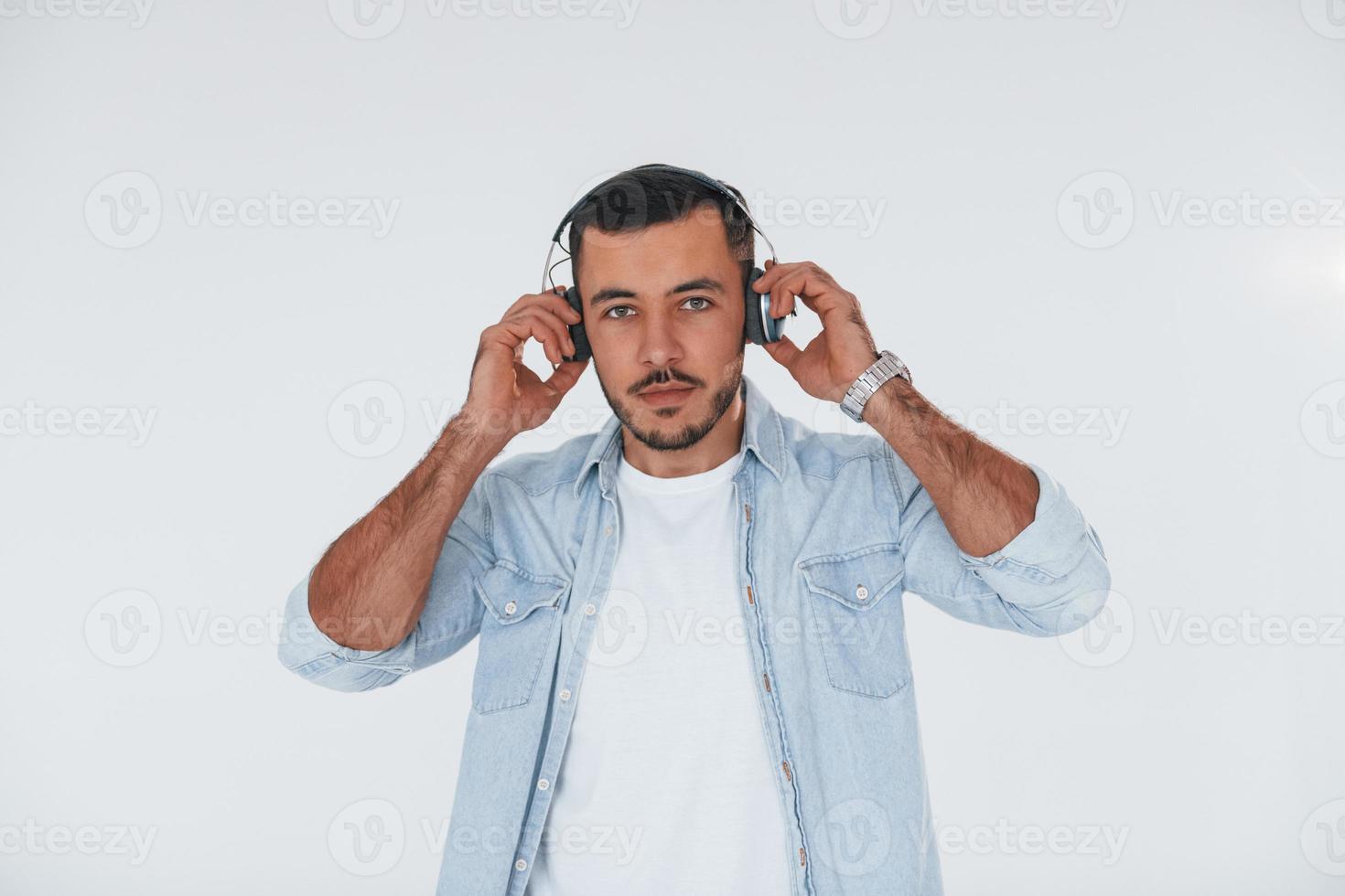 luistert naar de muziek- in koptelefoon. jong knap Mens staand binnenshuis tegen wit achtergrond foto