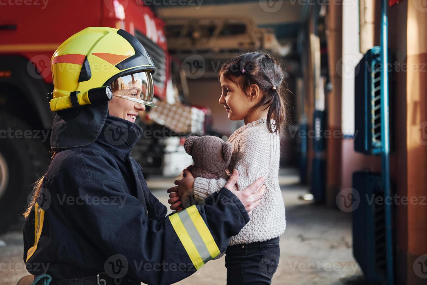 gelukkig weinig meisje is met vrouw brandweerman in beschermend uniform foto