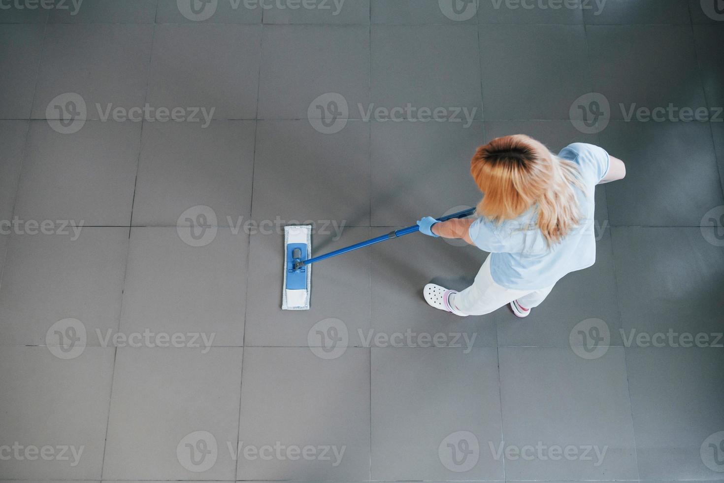 top visie van vrouw in blauw overhemd en beschermend handschoenen dat toepassingen vacuüm schoonmaakster foto