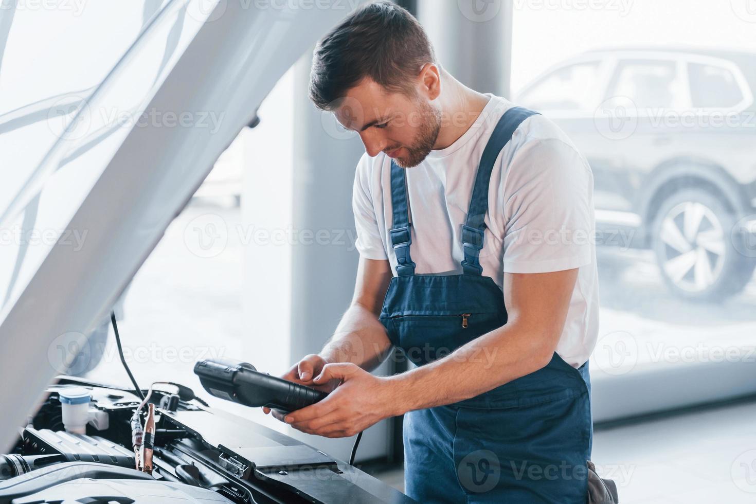 jong Mens in wit overhemd en blauw uniform reparaties auto- foto