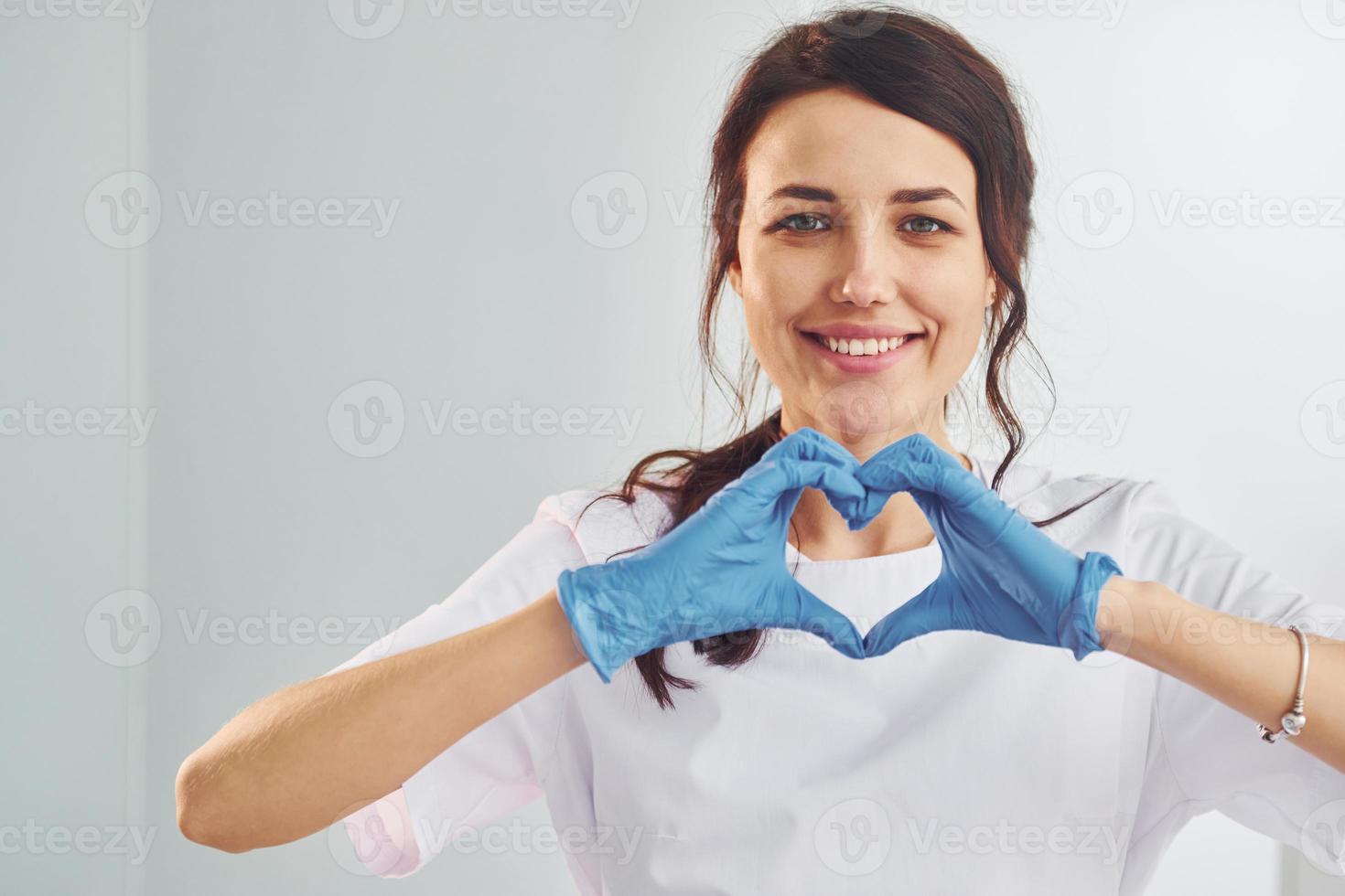 hart vormig gebaar. portret van professioneel vrouw tandarts met uitrusting dat staand binnenshuis foto