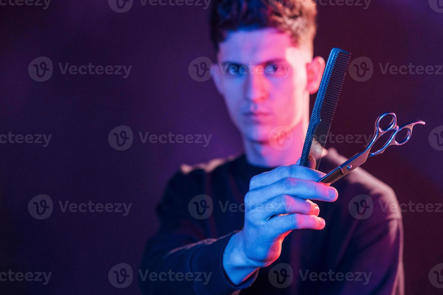 jong kapper met werk uitrusting staand in de studio met neon verlichting foto