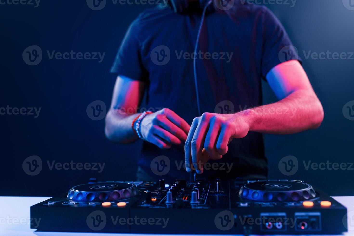 dichtbij omhoog visie van dj's handen dat werken met muziek- uitrusting in de club met neon verlichting foto