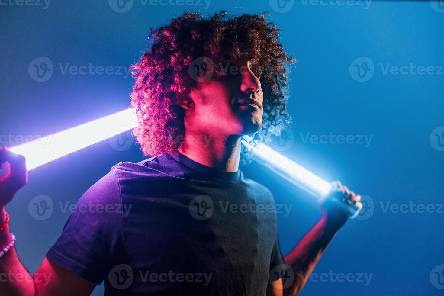 houdt verlichting apparatuur. jong mooi Mens met gekruld haar- is binnenshuis in de studio met neon verlichting foto