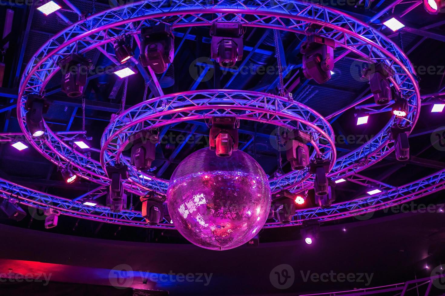 nacht disco club met neon blauw paars rood licht, disco spiegel bal en helder schijnwerper met ronde metaal kader lichtgevend bouw foto