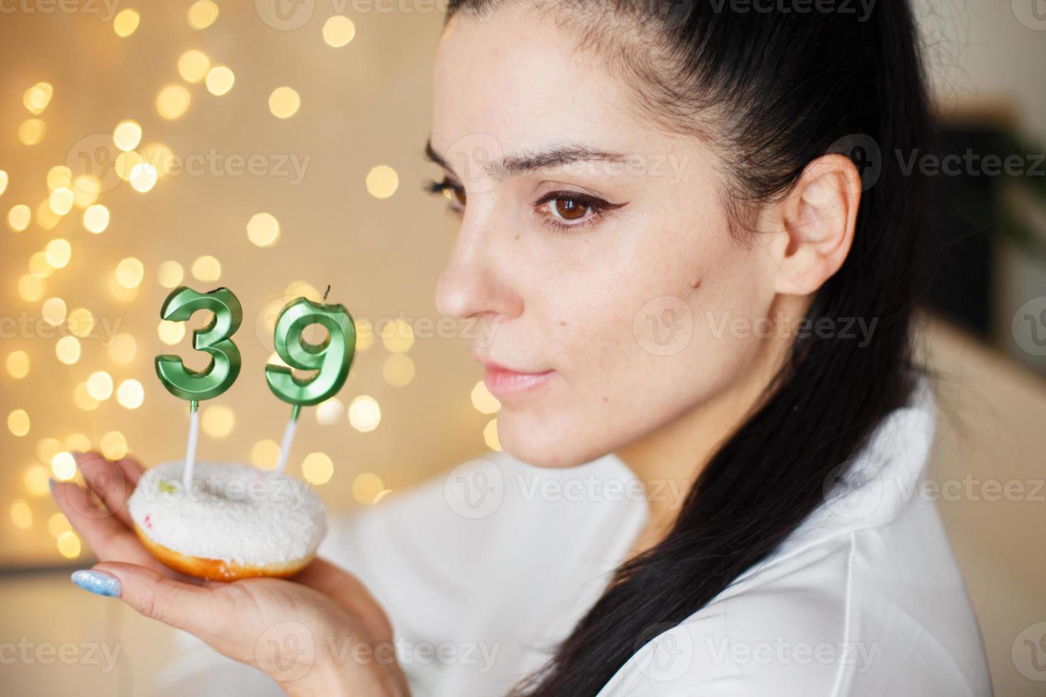 vrouw Holding een taart met de aantal 39 kaarsen Aan feestelijk wazig bokeh achtergrond foto