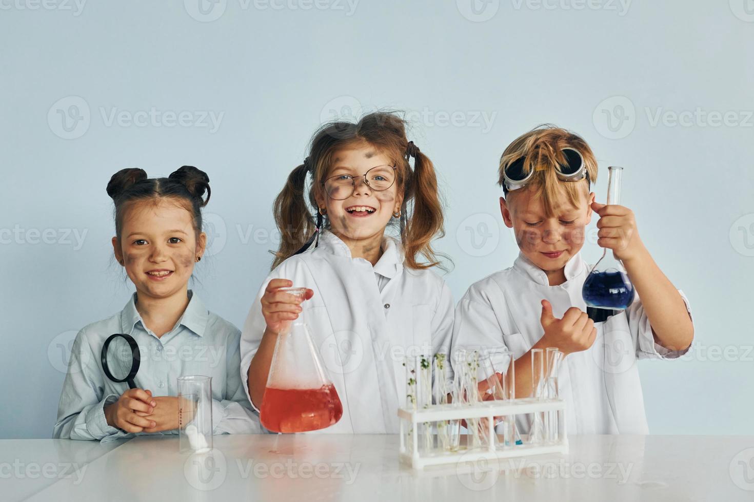 gelukkig vrienden lachend. kinderen in wit jassen Toneelstukken een wetenschappers in laboratorium door gebruik makend van uitrusting foto