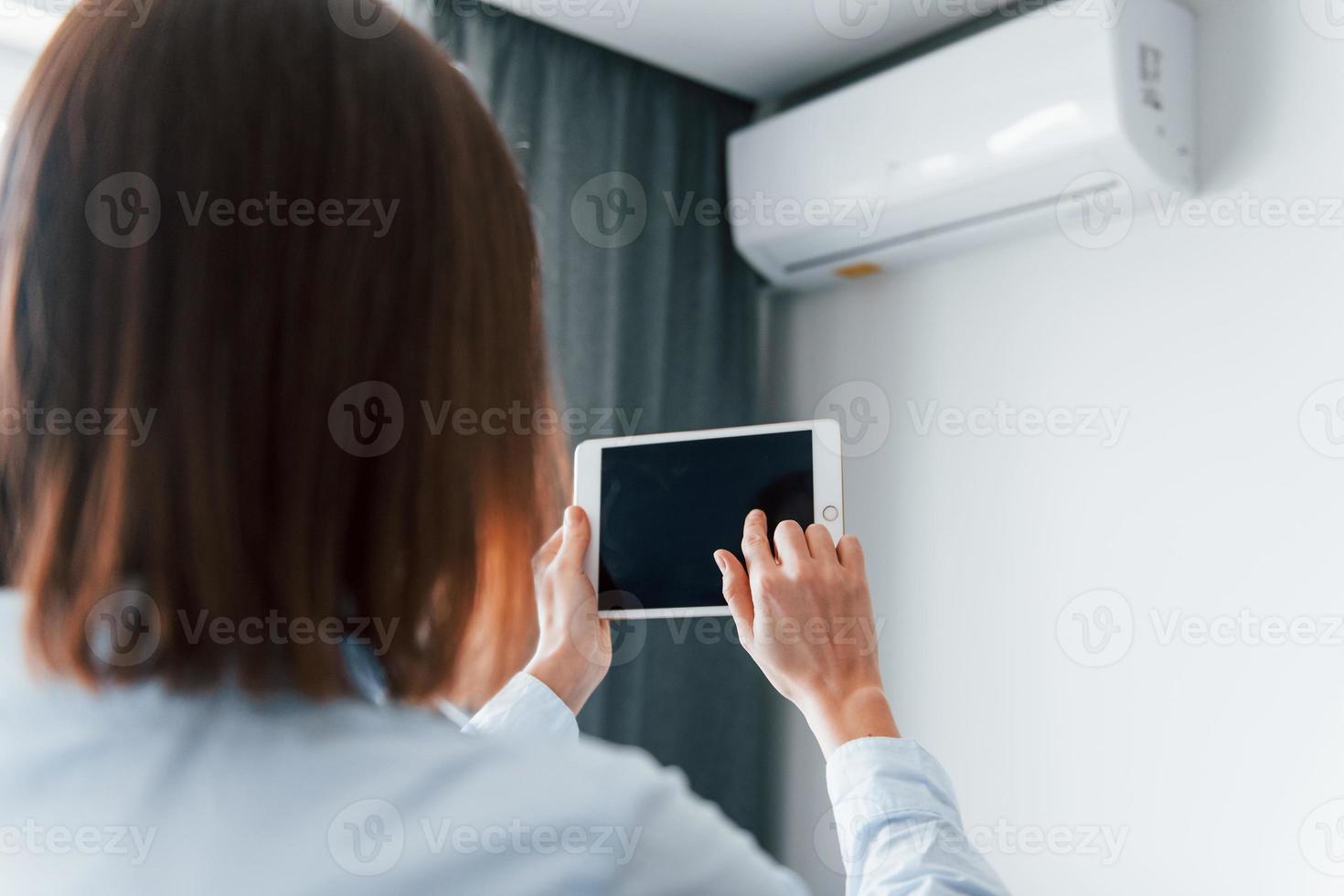 controlerend conditioner door tablet. jong vrouw is binnenshuis in kamer van modern huis Bij dag foto