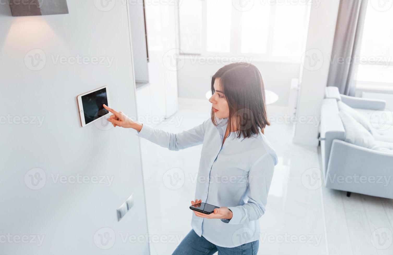 toepassingen tablet dat is gemonteerd in de muur. jong vrouw is binnenshuis in slim huis kamer Bij dag foto