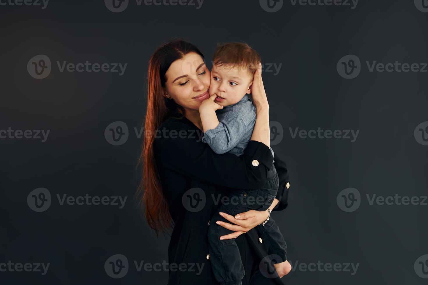 moeder in elegant zwart kleren is met haar weinig zoon in de studio foto