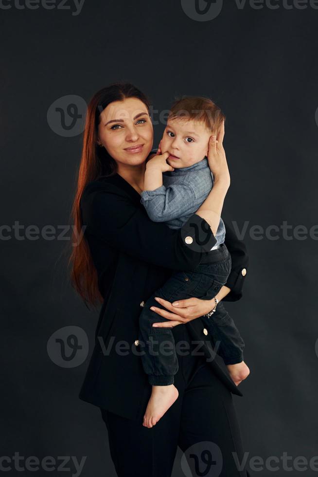 moeder in elegant zwart kleren is met haar weinig zoon in de studio foto