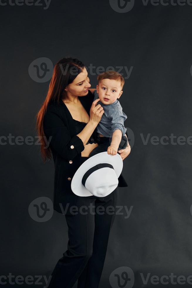 moeder in elegant zwart kleren is met haar weinig zoon in de studio foto