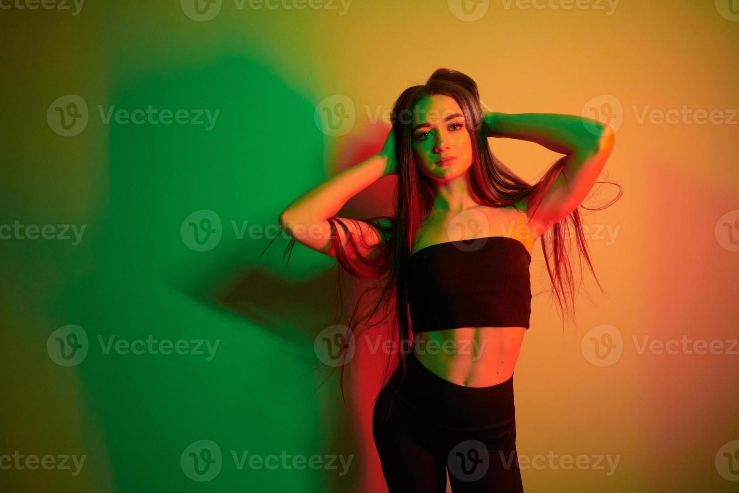 tegen muur. modieus jong vrouw staand in de studio met neon licht foto