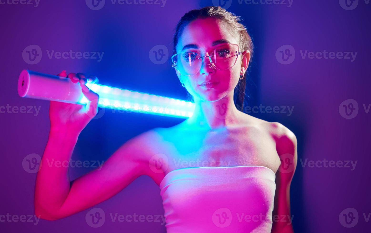 in bril. modieus jong vrouw staand in de studio met neon licht foto