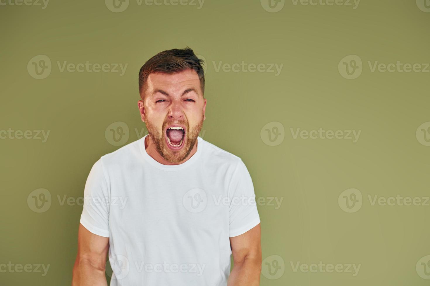 boos jong Mens in gewoontjes kleren staand binnenshuis in de studio foto