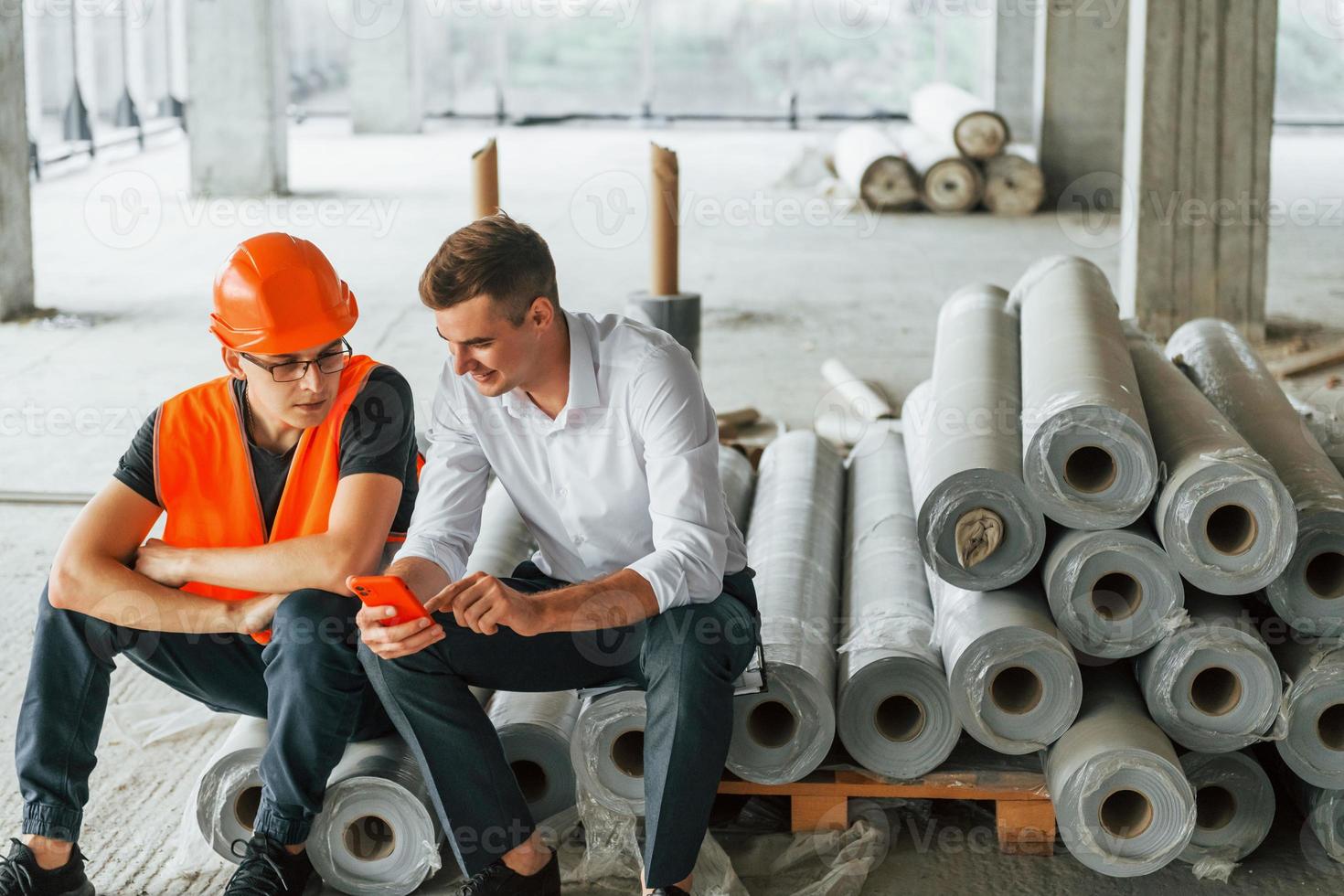 zittend Aan de materialen. Mens in pak en klusjesman in oranje beschermend slijtage is werken Aan bouw foto