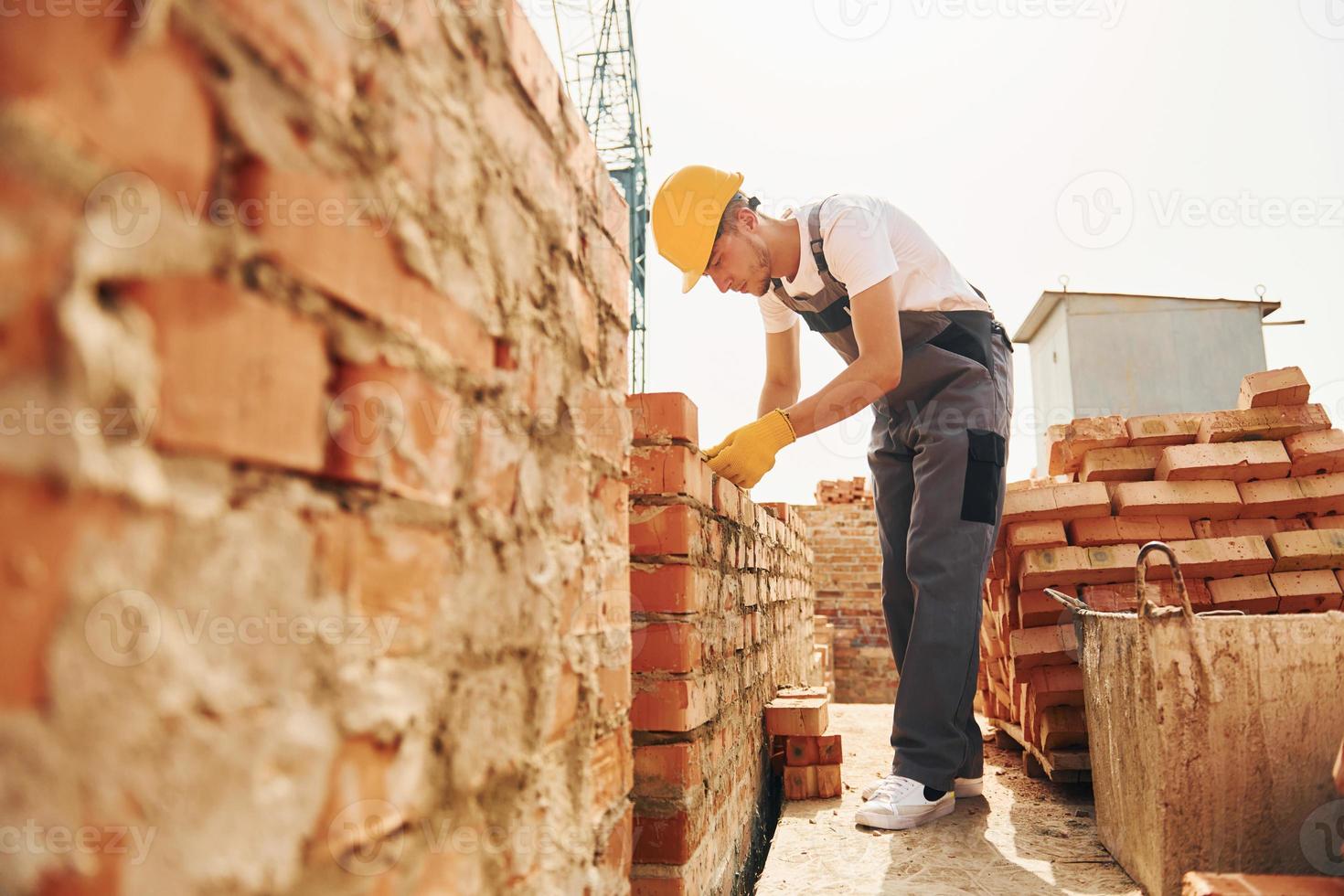 gebruik makend van bakstenen. jong bouw arbeider in uniform is bezig Bij de onvoltooid gebouw foto