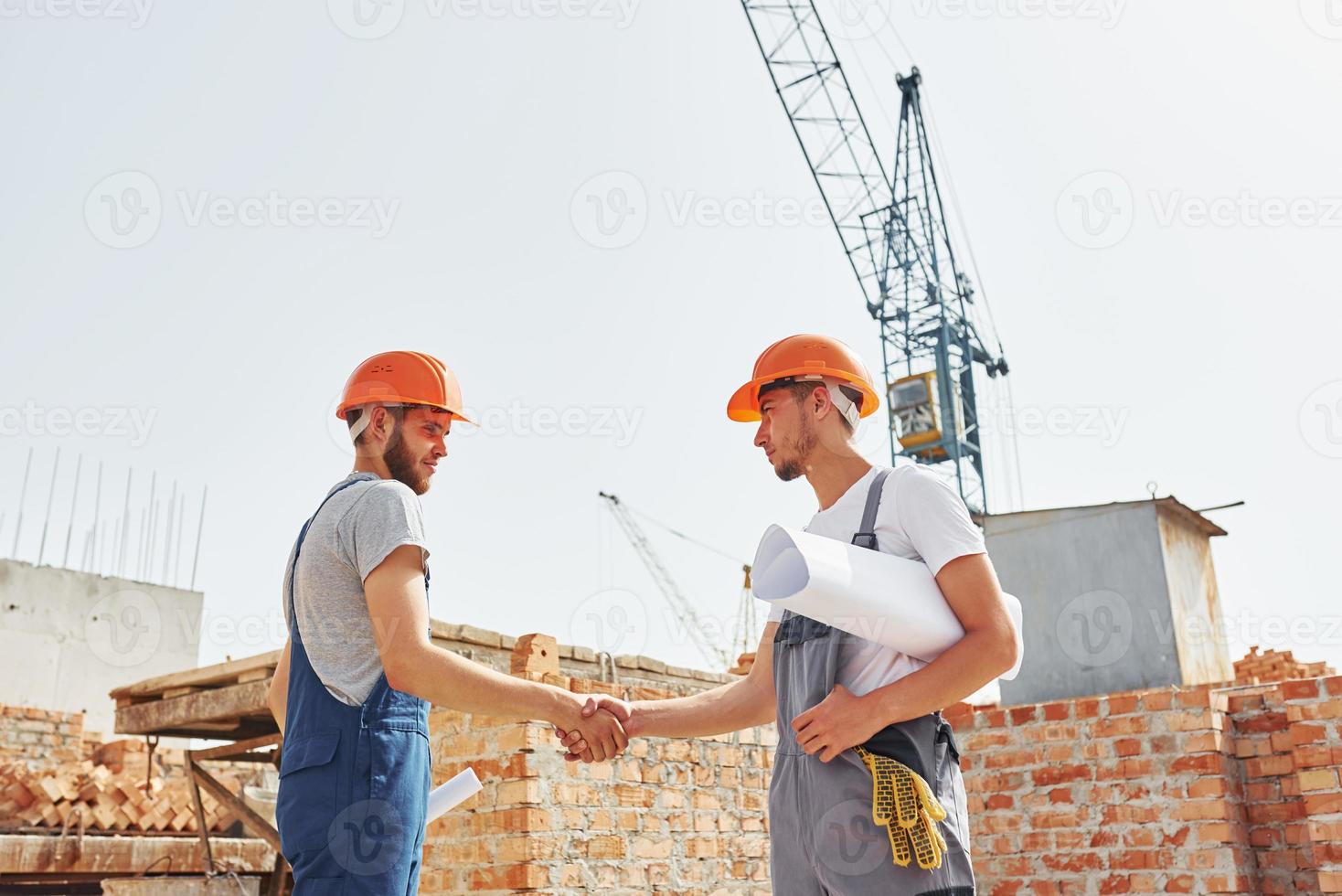 twee jong bouw arbeiders in uniformen is bezig Bij de onvoltooid gebouw foto